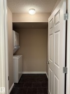 Washroom featuring stacked washer / drying machine, dark tile patterned floors, and a textured ceiling - 