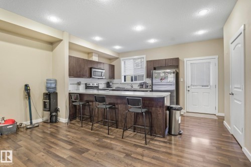 Kitchen with light countertops, a peninsula, appliances with stainless steel finishes, a breakfast bar area, and dark brown cabinetry - 30 6075 Schonsee Way, Edmonton, AB - Indoor Photo Showing Kitchen