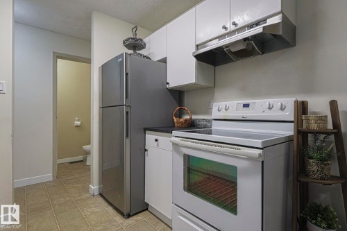 Kitchen featuring white electric range, dark countertops, under cabinet range hood, white cabinetry, and a textured ceiling - 51 Belmead Gardens, Edmonton, AB - Indoor