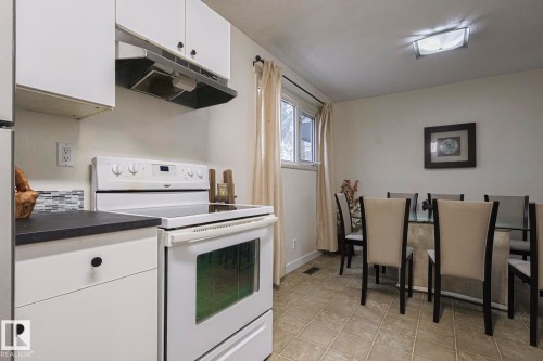 Kitchen with electric stove, white cabinetry, under cabinet range hood, dark countertops, and light tile patterned floors - 51 Belmead Gardens, Edmonton, AB - Indoor Photo Showing Kitchen