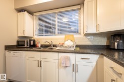 Kitchen with dark countertops, white dishwasher, stainless steel microwave, white cabinets, and tasteful backsplash - 