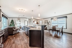 Kitchen featuring hanging light fixtures, dark brown cabinets, ornamental molding, a center island with sink, and plenty of natural light - 