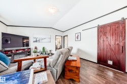 Living area with a barn door, lofted ceiling, wood finished floors, and ornamental molding - 