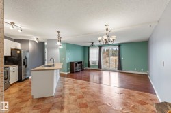 Kitchen featuring decorative light fixtures, open floor plan, an island with sink, white cabinets, and a textured ceiling - 
