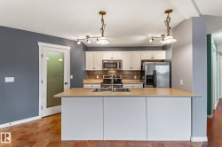 Kitchen featuring white cabinets, stainless steel appliances, decorative backsplash, hanging light fixtures, and light countertops - 