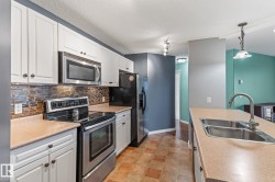 Kitchen featuring stainless steel appliances, tasteful backsplash, white cabinetry, hanging light fixtures, and a textured ceiling - 