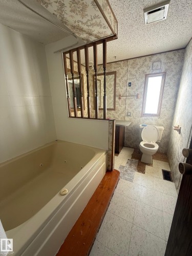 Bathroom featuring a built-in tub, toilet, and vanity with an overhead mirror - 4904 51 Avenue, Opal, AB - Indoor Photo Showing Bathroom