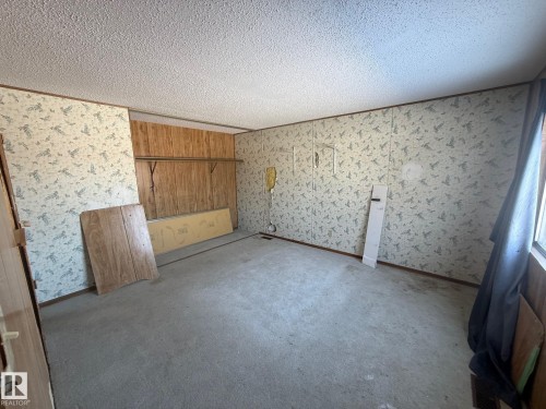 The property features a room with textured ceilings, carpeting, and walls adorned with wallpaper and wood paneling - 4904 51 Avenue, Opal, AB -  Photo Showing Other Room