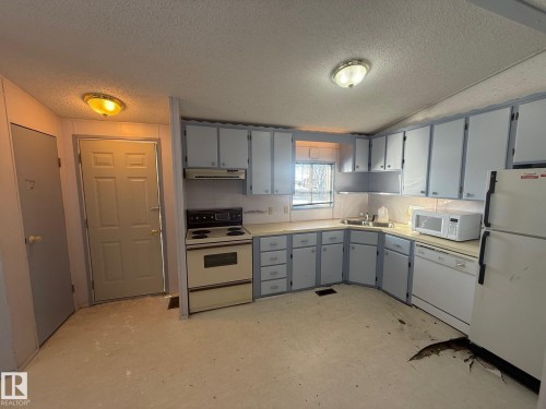 The property features a kitchen with light-colored cabinetry and countertops, a window above the sink, and a white refrigerator and dishwasher - 4904 51 Avenue, Opal, AB - Indoor Photo Showing Kitchen With Double Sink