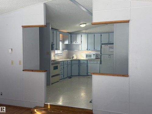 The kitchen features light blue cabinetry, white countertops, and white appliances, including a microwave, refrigerator, stove, and dishwasher - 4904 51 Avenue, Opal, AB - Indoor Photo Showing Kitchen