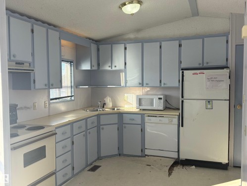 The kitchen features light-colored cabinetry and countertops, a built-in sink, and a window with blinds - 4904 51 Avenue, Opal, AB - Indoor Photo Showing Kitchen With Double Sink