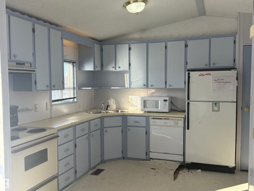 The kitchen features ample cabinetry, a double basin sink, and white appliances including a refrigerator, dishwasher, and microwave - 4904 51 Avenue, Opal, AB - Indoor Photo Showing Kitchen With Double Sink