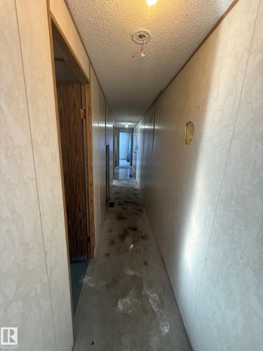 A long hallway featuring light-colored paneling, a visible light fixture on the ceiling, and a doorway leading into a separate area - 4904 51 Avenue, Opal, AB - Indoor Photo Showing Other Room