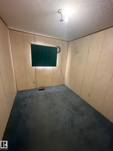 The property features a room with light-colored paneled walls and a blue carpet - 4904 51 Avenue, Opal, AB - Indoor Photo Showing Other Room