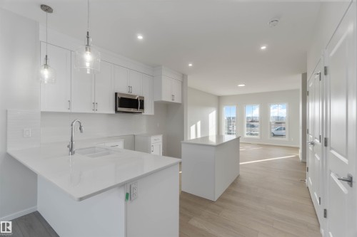Kitchen featuring a center island, white cabinets, stainless steel microwave, decorative light fixtures, and light stone countertops - 262 Chappelle Drive, Edmonton, AB - Indoor Photo Showing Kitchen With Upgraded Kitchen