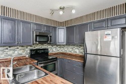 Kitchen with stainless steel appliances, wood counters, a textured ceiling, gray cabinets, and decorative backsplash - 