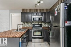 Kitchen with appliances with stainless steel finishes, a peninsula, light tile patterned flooring, wooden counters, and decorative backsplash - 