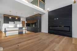 Kitchen with a center island with sink, a large fireplace, pendant lighting, light wood finished floors, and a towering ceiling - 