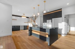 Kitchen featuring dark cabinets, an island with sink, light wood-style floors, decorative light fixtures, and modern cabinets - 