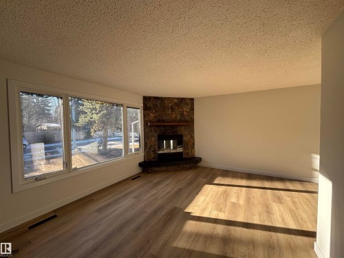 Unfurnished living room with a stone fireplace, wood finished floors, and a textured ceiling - 11744 37 Avenue, Edmonton, AB - Indoor Photo Showing Living Room With Fireplace