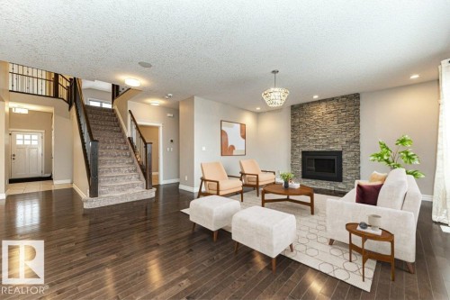 Living area with stairs, a fireplace, a textured ceiling, dark wood-type flooring, and a chandelier - 3198 Winspear Crescent Sw, Edmonton, AB - Indoor Photo Showing Living Room With Fireplace