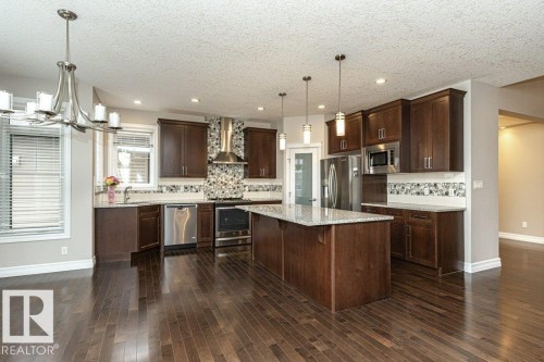 Kitchen with dark brown cabinets, stainless steel appliances, pendant lighting, a chandelier, and wall chimney exhaust hood - 3198 Winspear Crescent Sw, Edmonton, AB - Indoor Photo Showing Kitchen With Stainless Steel Kitchen With Upgraded Kitchen