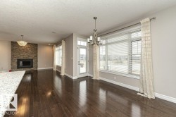 Unfurnished living room with a textured ceiling, a chandelier, dark wood-type flooring, and a stone fireplace - 