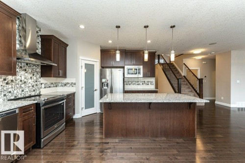 Kitchen featuring wall chimney exhaust hood, stainless steel appliances, dark brown cabinetry, light stone counters, and recessed lighting - 3198 Winspear Crescent Sw, Edmonton, AB - Indoor Photo Showing Kitchen With Upgraded Kitchen