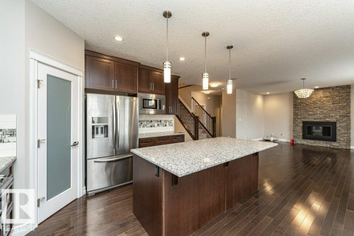 Kitchen with dark brown cabinetry, stainless steel appliances, light stone countertops, decorative light fixtures, and a kitchen island - 3198 Winspear Crescent Sw, Edmonton, AB - Indoor Photo Showing Kitchen With Stainless Steel Kitchen With Upgraded Kitchen