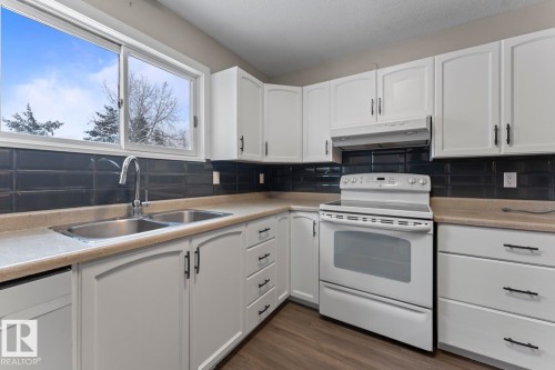 Kitchen featuring white cabinets, electric range, under cabinet range hood, light countertops, and backsplash - 4719 47 Avenue, Cold Lake, AB - Indoor Photo Showing Kitchen With Double Sink