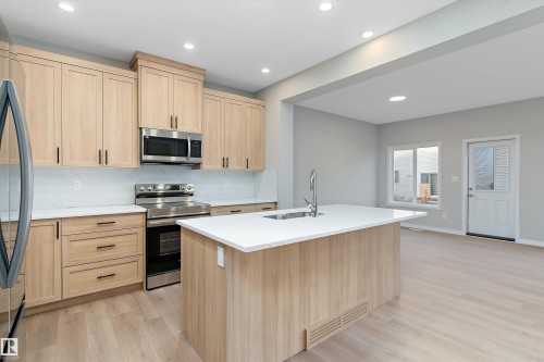 Kitchen with light brown cabinetry, appliances with stainless steel finishes, recessed lighting, light wood-style flooring, and a center island with sink - 6320 King Wynd, Edmonton, AB - Indoor Photo Showing Kitchen With Double Sink