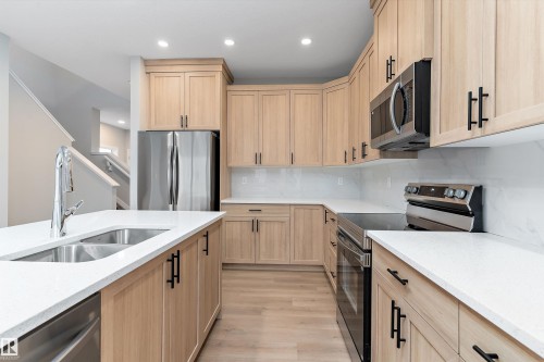Kitchen with light brown cabinetry, stainless steel appliances, light stone countertops, backsplash, and light wood finished floors - 6320 King Wynd, Edmonton, AB - Indoor Photo Showing Kitchen With Double Sink With Upgraded Kitchen