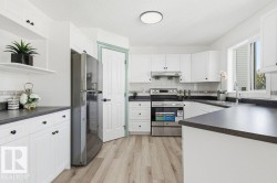 Kitchen with stainless steel appliances, dark countertops, white cabinets, light wood finished floors, and a textured ceiling - 