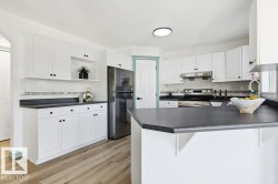Kitchen featuring appliances with stainless steel finishes, white cabinetry, dark countertops, a peninsula, and a textured ceiling - 