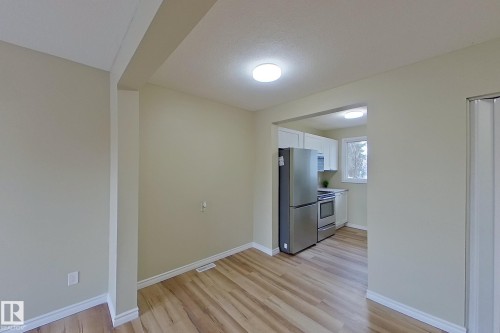 Kitchen featuring appliances with stainless steel finishes, white cabinets, light wood finished floors, a textured ceiling, and light countertops - 112 Dickinsfield Court Nw, Edmonton, AB - Indoor