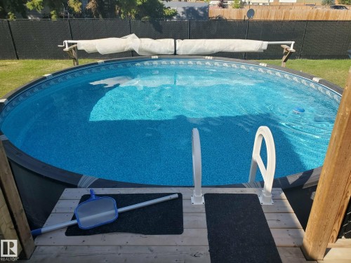 The property features an outdoor swimming pool with an attached deck, complete with white entry steps and a rolled-up pool cover - 5510 Railway Avenue, Glendon, AB - Outdoor With Above Ground Pool With Backyard