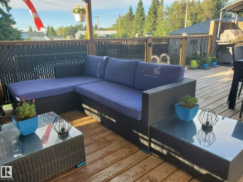 Spacious wooden deck featuring a privacy fence, a corner sectional with blue cushions, and glass-top tables - 5510 Railway Avenue, Glendon, AB - Outdoor With Deck Patio Veranda With Exterior