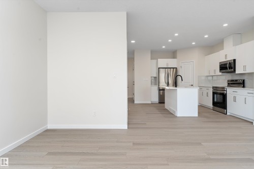 Kitchen featuring a kitchen island with sink, appliances with stainless steel finishes, white cabinetry, light wood-style flooring, and backsplash - 823 Rowan Close, Edmonton, AB - Indoor Photo Showing Kitchen With Upgraded Kitchen