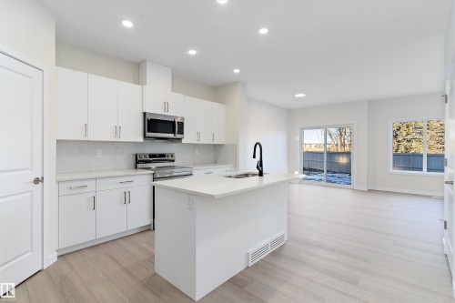 Kitchen featuring white cabinets, appliances with stainless steel finishes, a kitchen island with sink, light wood finished floors, and decorative backsplash - 823 Rowan Close, Edmonton, AB - Indoor Photo Showing Kitchen With Upgraded Kitchen