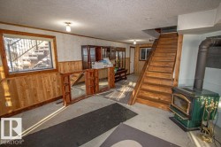Living area featuring wooden walls, a wood stove, stairs, wainscoting, and a textured ceiling - 