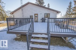 Snow covered house featuring a wooden deck, stucco siding, and stairway - 