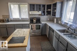 Kitchen featuring a freestanding wood-finish island, gray cabinetry, white countertops, and a patterned tile backsplash - 