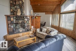 Spacious living area featuring a prominent stone fireplace, vaulted wood-plank ceiling, and wood-paneled walls - 