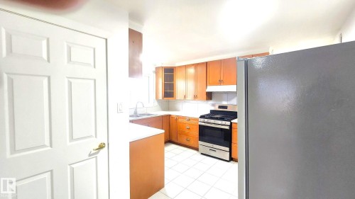 Kitchen featuring appliances with stainless steel finishes, light countertops, glass insert cabinets, brown cabinets, and under cabinet range hood - 11516 133A Avenue, Edmonton, AB - Indoor Photo Showing Kitchen
