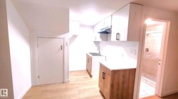 Kitchen featuring light countertops, white cabinetry, under cabinet range hood, and light wood-style floors - 