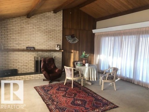Living area with a fireplace, wood ceiling, carpet flooring, and wooden walls - 4213 42 Avenue, Innisfail, AB - Indoor