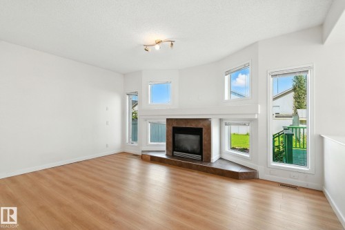 Unfurnished living room with a tiled fireplace, light wood-type flooring, and a textured ceiling - 7836 7 Avenue, Edmonton, AB - Indoor Photo Showing Living Room With Fireplace
