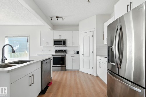 Kitchen with stainless steel appliances, white cabinets, a textured ceiling, and light wood finished floors - 7836 7 Avenue, Edmonton, AB - Indoor Photo Showing Kitchen With Double Sink With Upgraded Kitchen