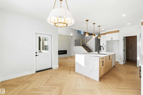Two tone kitchen with a center island with sink, light stone counters, parquet flooring, a glass covered fireplace, and two tone cabinetry - 94 Eldridge Pointe, St. Albert, AB - Indoor Photo Showing Kitchen