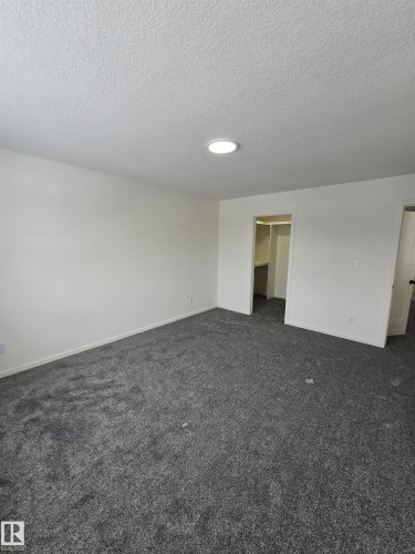 Unfurnished bedroom with dark carpet, a spacious closet, and a textured ceiling - 7706 174A Avenue, Edmonton, AB - Indoor Photo Showing Other Room